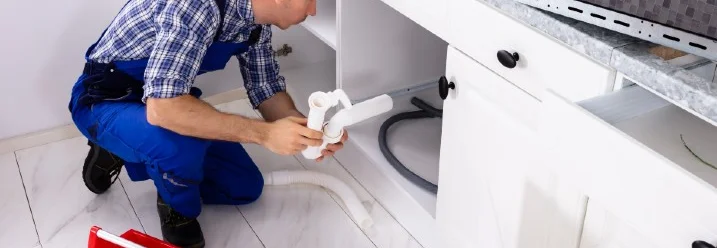 Person repariert Siphon unter Spüle